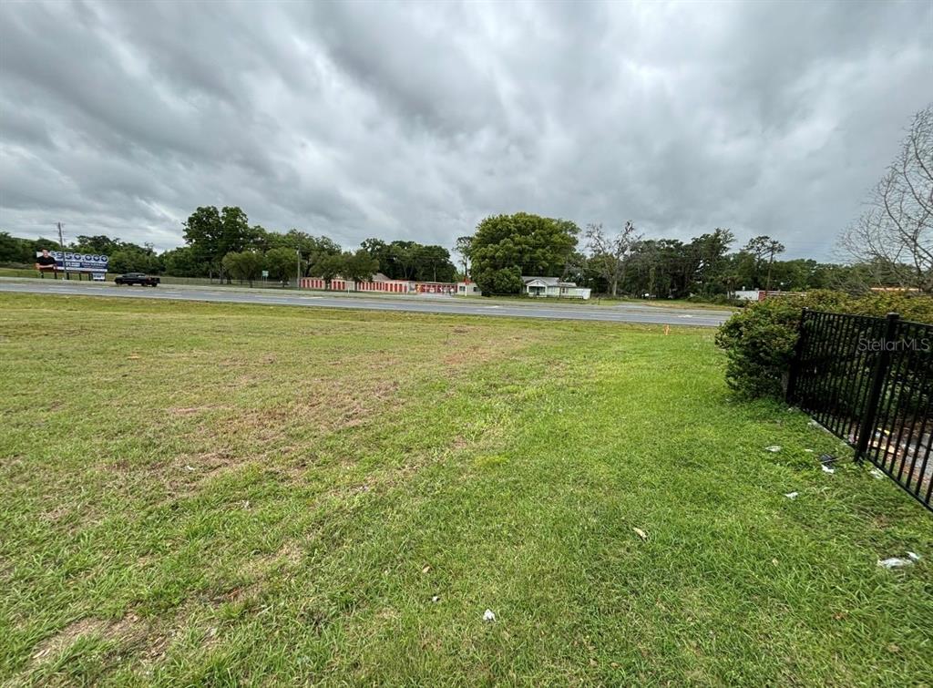 A grassy vacant lot sits in front of a road with trees and buildings beyond — TBT SE HWY 484 HIGHWAY SE, BELLEVIEW, FL