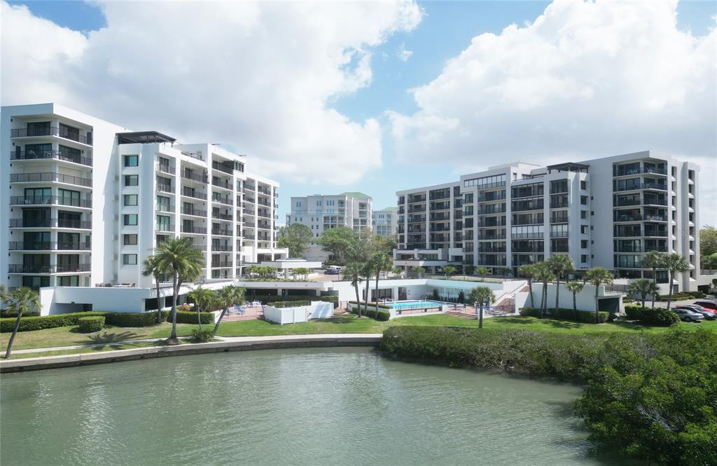 An exterior view of two white multi-story apartment buildings overlooking a canal and swimming pool — 8 BELLEVIEW BOULEVARD UNIT 702, BELLEAIR, FL