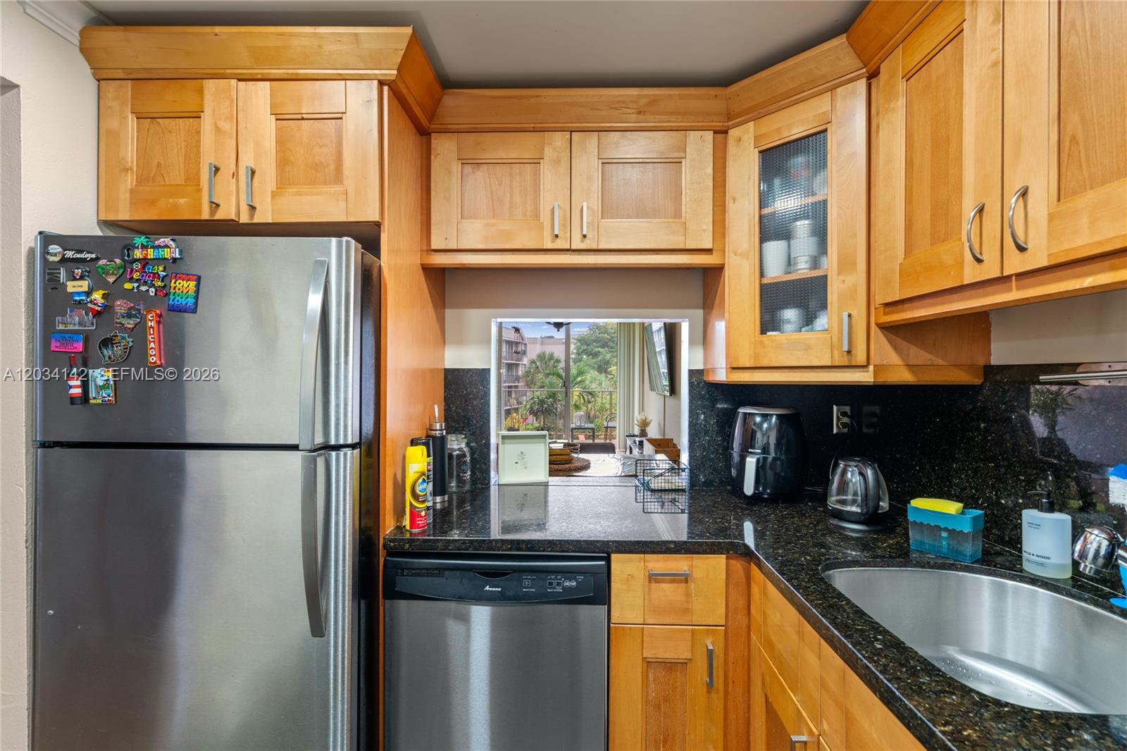 A kitchen features wood cabinets, dark granite countertops, stainless steel appliances, and a pass-through window — 13120 SW 92nd Ave # 313, Miami FL 33176, MIAMI, FL