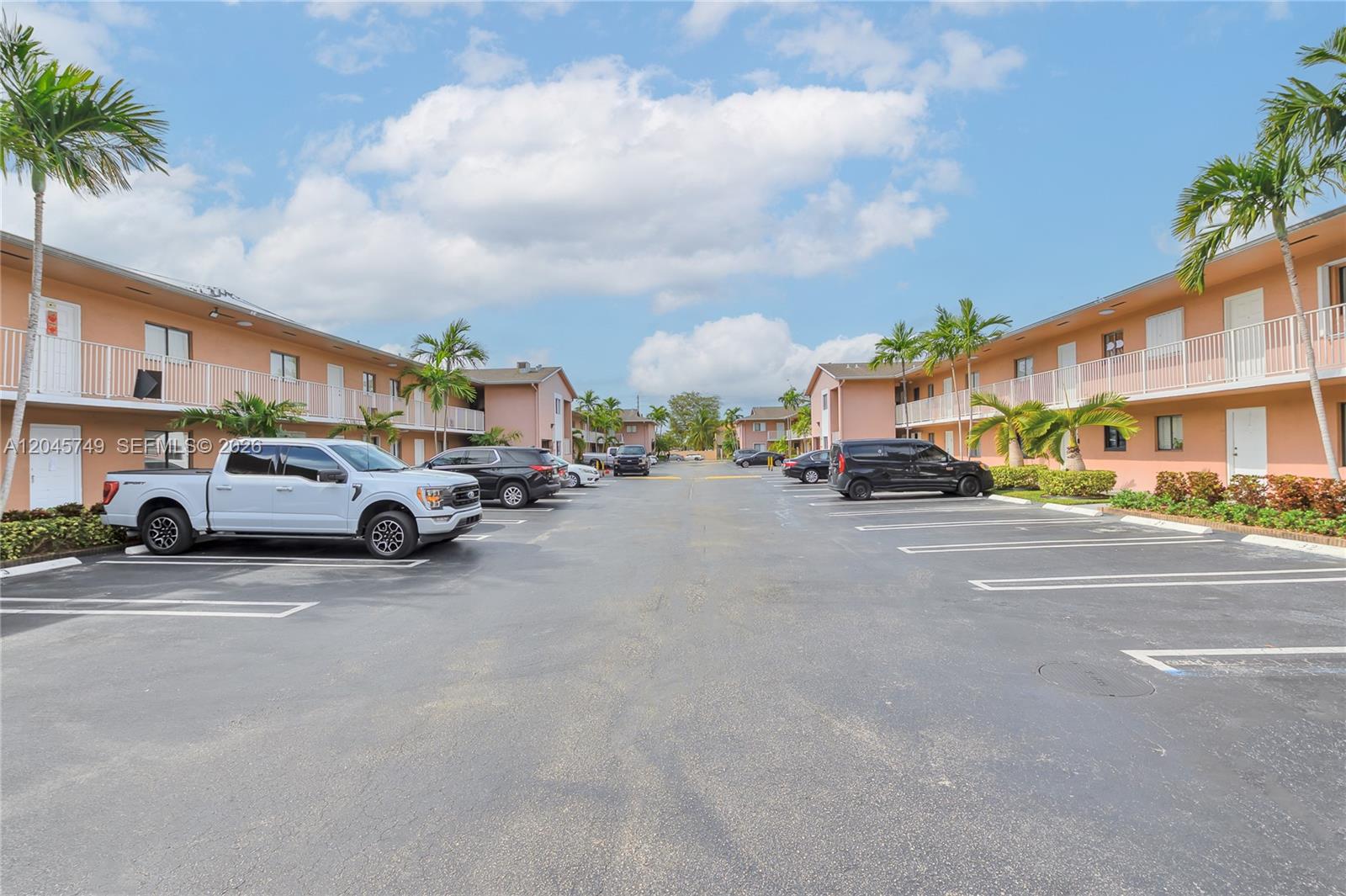 A parking lot sits between two two-story apartment buildings with palm trees and balconies — 6041 W 24th Ave # 111, Hialeah FL 33016, HIALEAH, FL