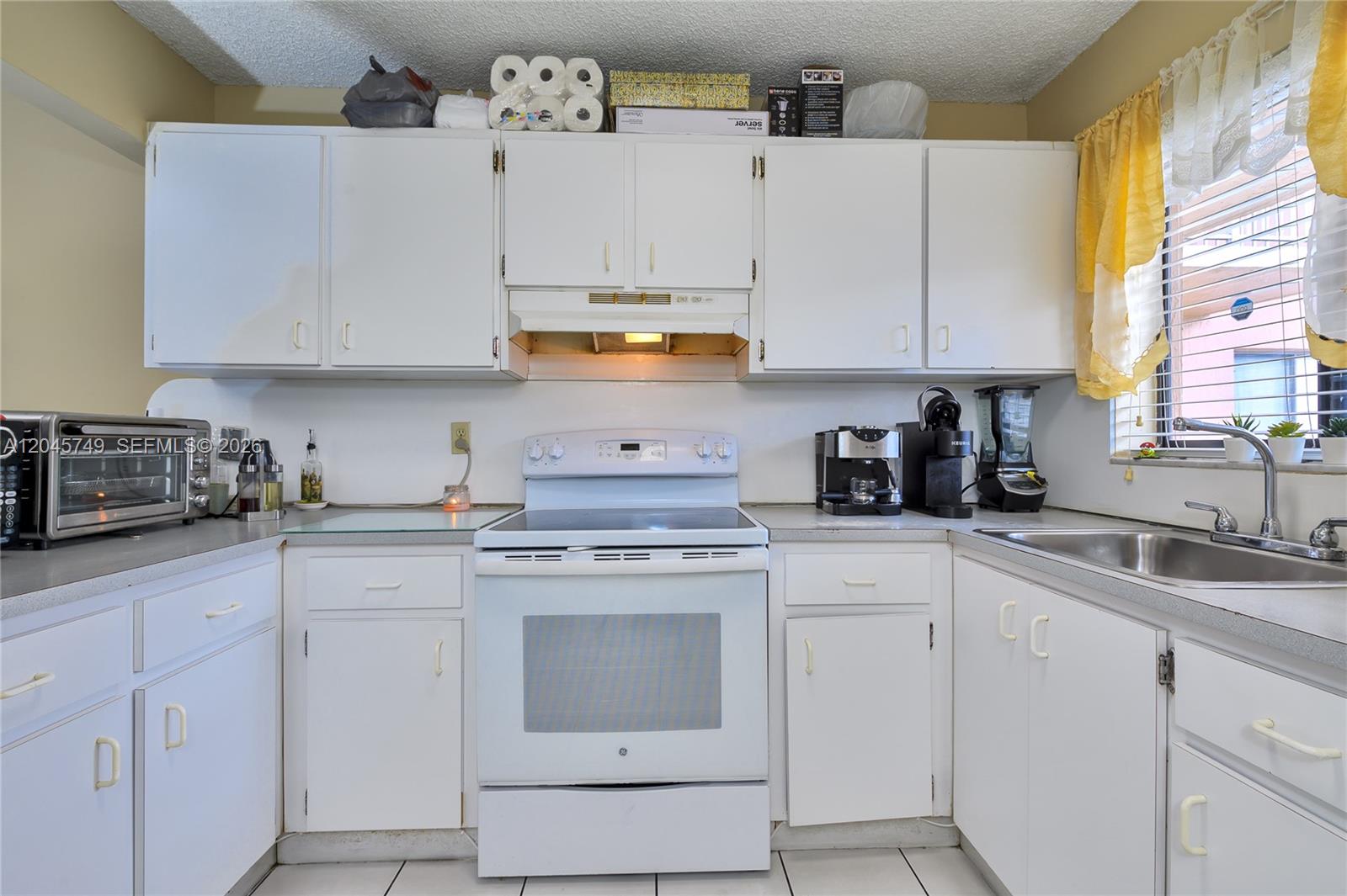 A kitchen features white cabinets, a white electric stove, and a stainless steel sink — 6041 W 24th Ave # 111, Hialeah FL 33016, HIALEAH, FL
