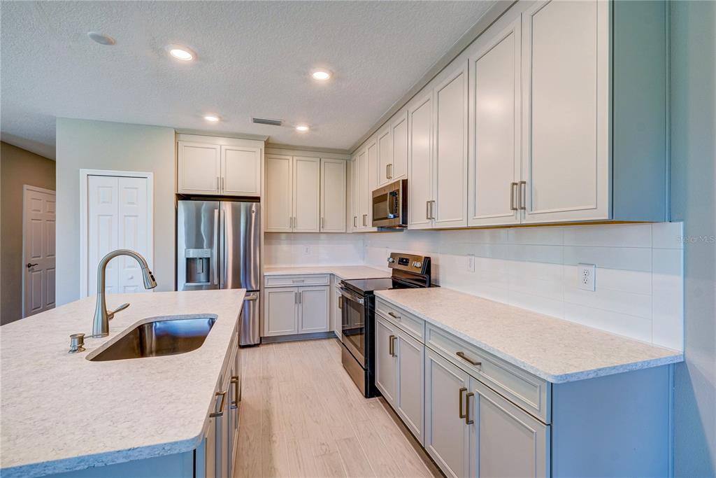 A kitchen features light gray cabinets, white countertops, stainless steel appliances, and a central island — 5512 TRIPOLI DRIVE, PALMETTO, FL