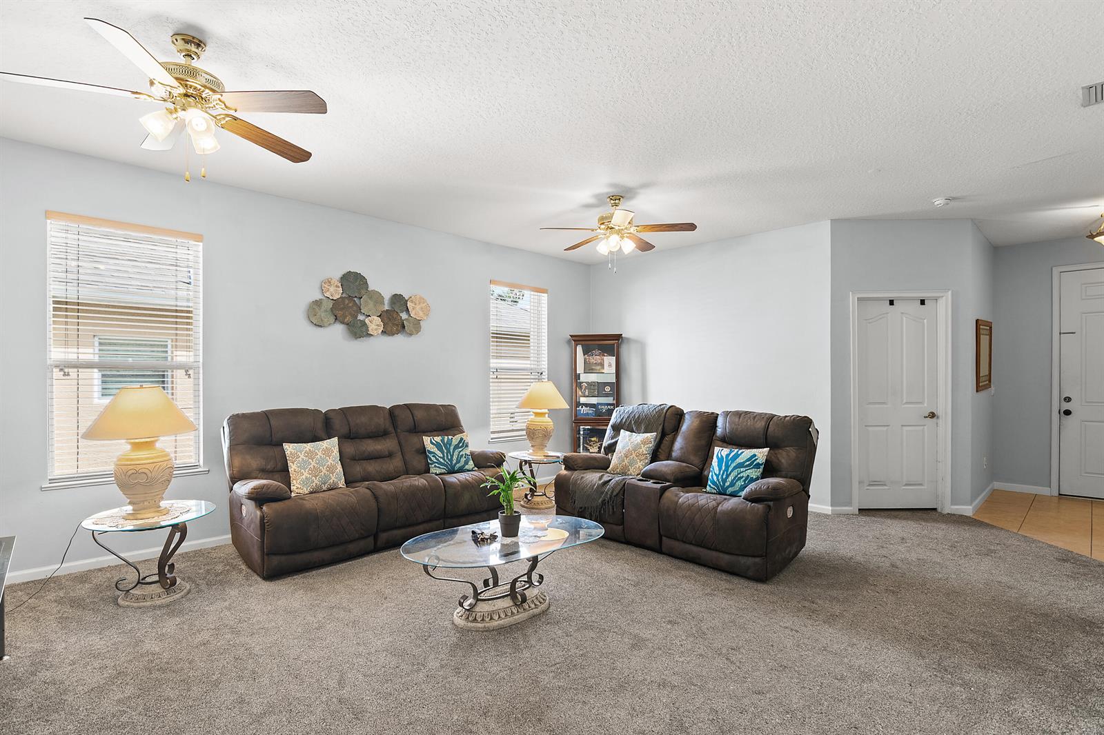 A living room features two brown reclining sofas, a glass coffee table, and two ceiling fans — 504 Sebastian Crossing Boulevard, Sebastian FL 32958, SEBASTIAN, FL