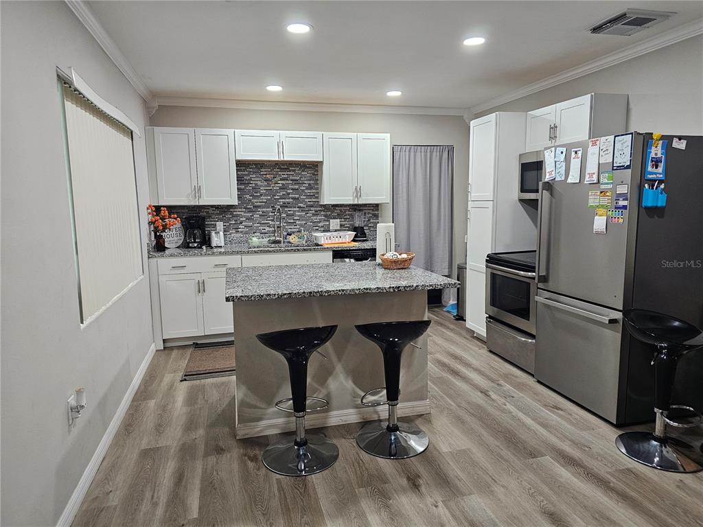 A kitchen features white cabinets, granite countertops, a central island with two stools, and stainless appliances — 2117 IVEY LANE, LAKELAND, FL
