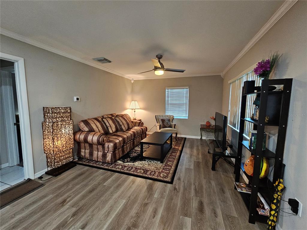 A living room features wood-look flooring, a striped sofa, a ceiling fan, and a shelving unit — 2117 IVEY LANE, LAKELAND, FL