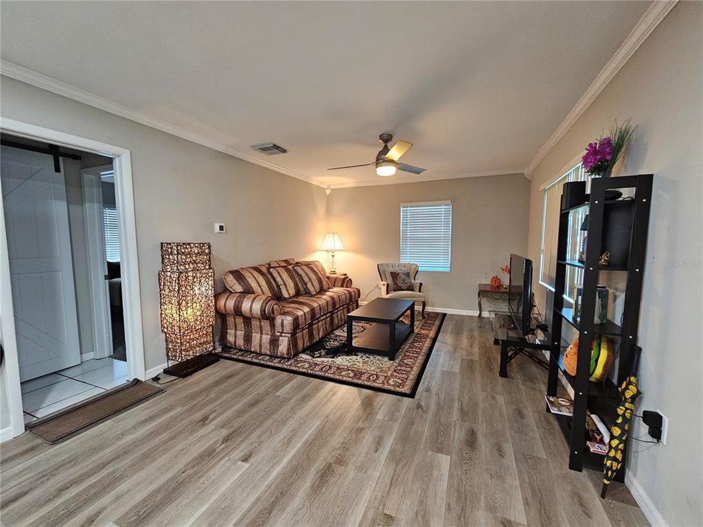 A living room features wood-look flooring, a striped sofa, a ceiling fan, and a bookshelf — 2117 IVEY LANE, LAKELAND, FL