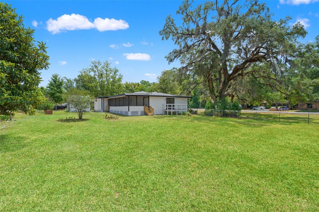 A white single-story house with a screened-in porch sits on a large, grassy lot — 16119 WILSON BOULEVARD, BROOKSVILLE, FL