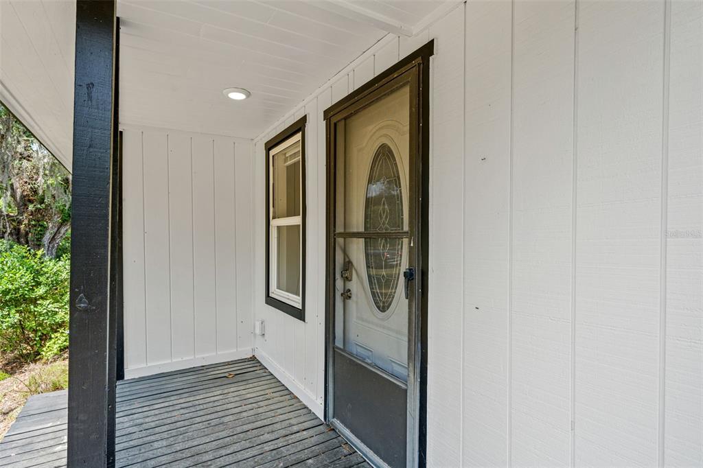 A covered wooden porch features a white exterior wall, a window, and a screen door — 16119 WILSON BOULEVARD, BROOKSVILLE, FL