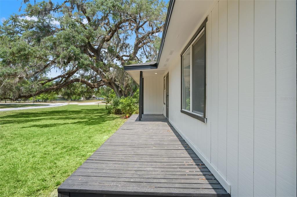 A wooden porch runs along the side of a white house with a large oak tree — 16119 WILSON BOULEVARD, BROOKSVILLE, FL