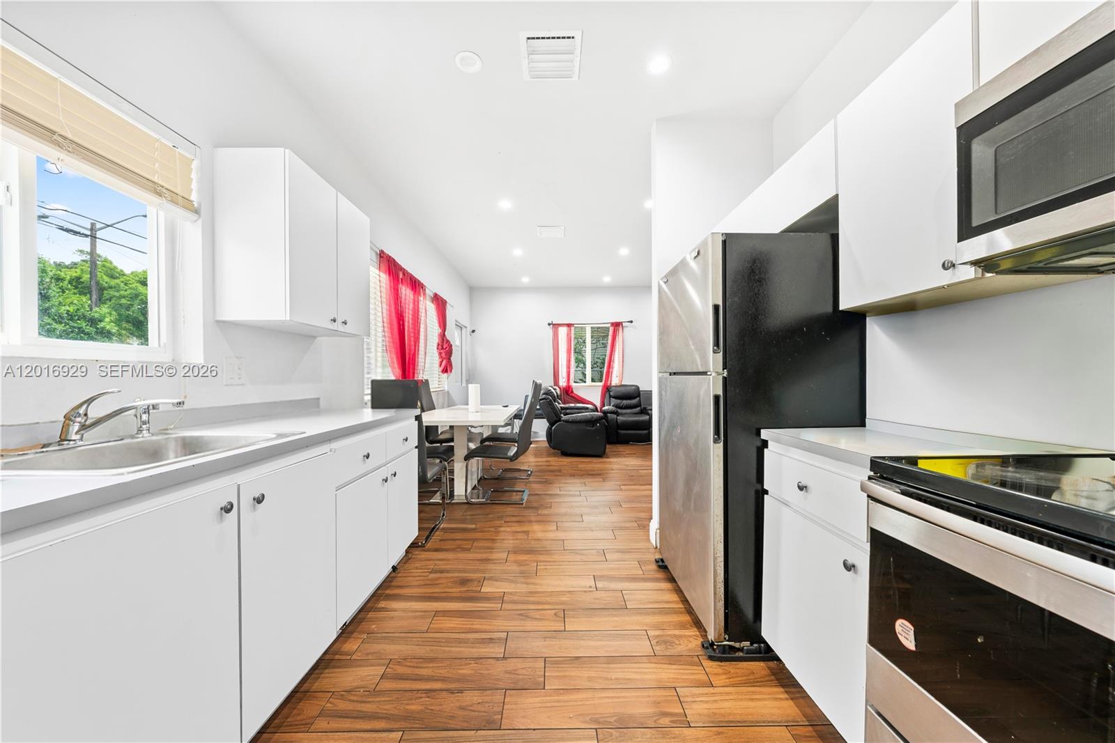 A kitchen with white cabinets and stainless steel appliances leads into a dining and living area — 4721 NW 15th Ct # 1, Miami FL 33142, MIAMI, FL