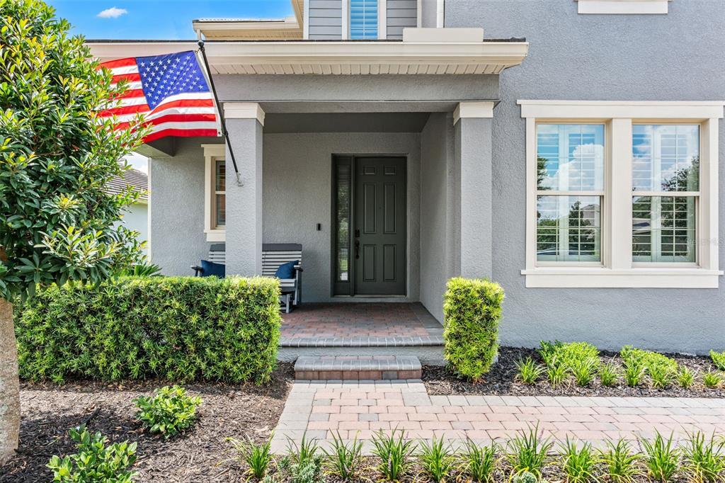 A gray house exterior features a covered porch, a brick walkway, and an American flag — 10198 MERRYMEETING BAY DRIVE, WINTER GARDEN, FL