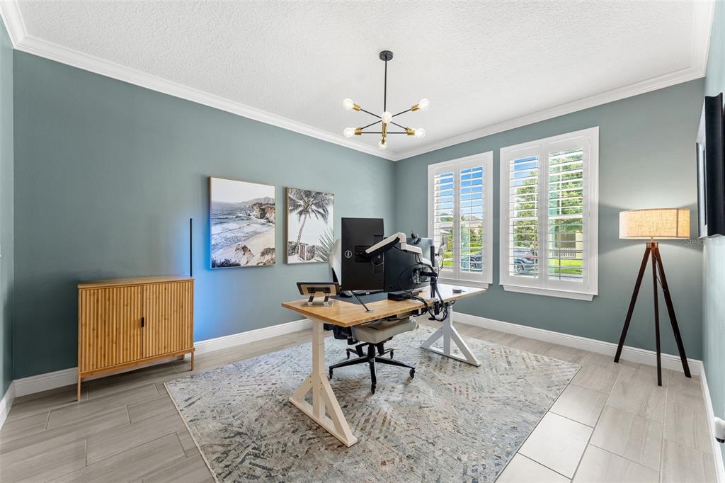 A home office features a wooden desk, blue walls, a rug, and a modern light fixture — 10198 MERRYMEETING BAY DRIVE, WINTER GARDEN, FL