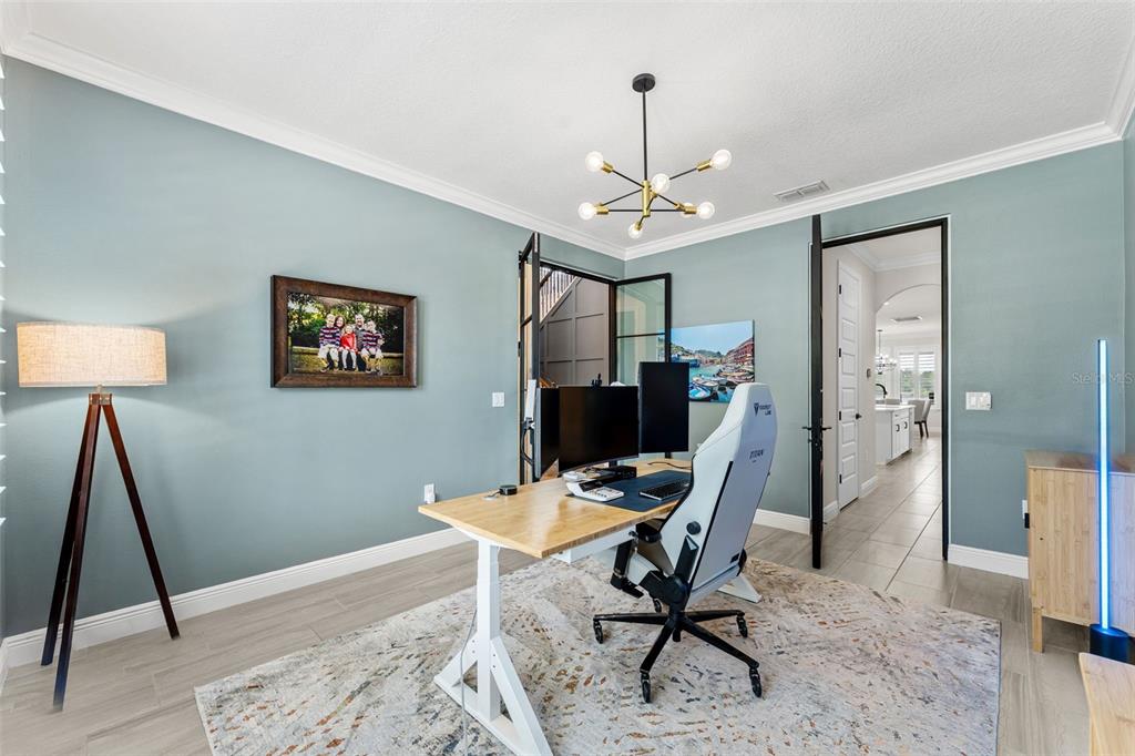 A home office features light blue walls, a wooden desk, a gaming chair, and a chandelier — 10198 MERRYMEETING BAY DRIVE, WINTER GARDEN, FL