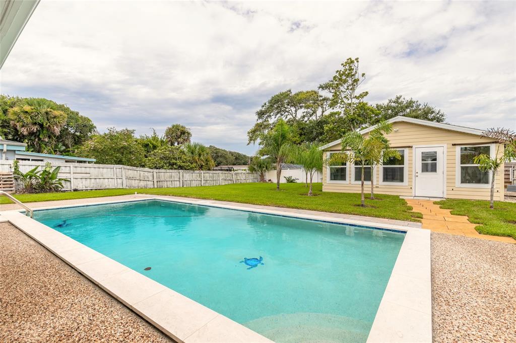 A backyard features a rectangular swimming pool, a grassy lawn, and a light-colored detached building — 808 E 16TH AVENUE, NEW SMYRNA BEACH, FL