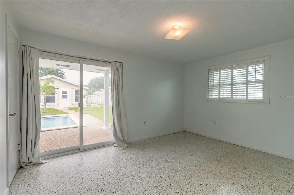 A bedroom with white walls, speckled flooring, a sliding glass door, and a backyard pool view — 808 E 16TH AVENUE, NEW SMYRNA BEACH, FL