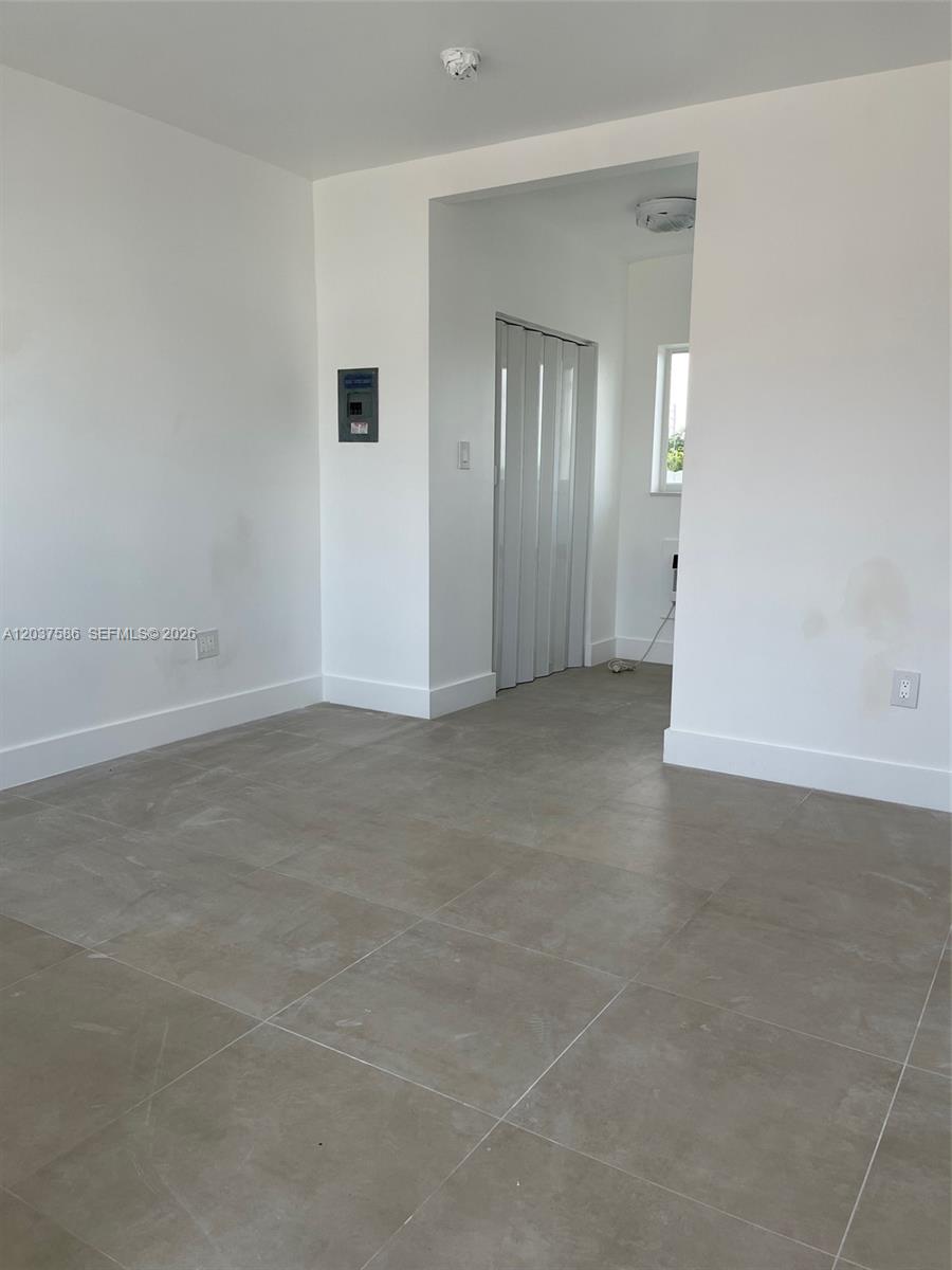 An empty room features light gray tile flooring, white walls, and a folding closet door — 2196 Ali Baba Ave # 6, Opa-Locka FL 33054, OPA-LOCKA, FL