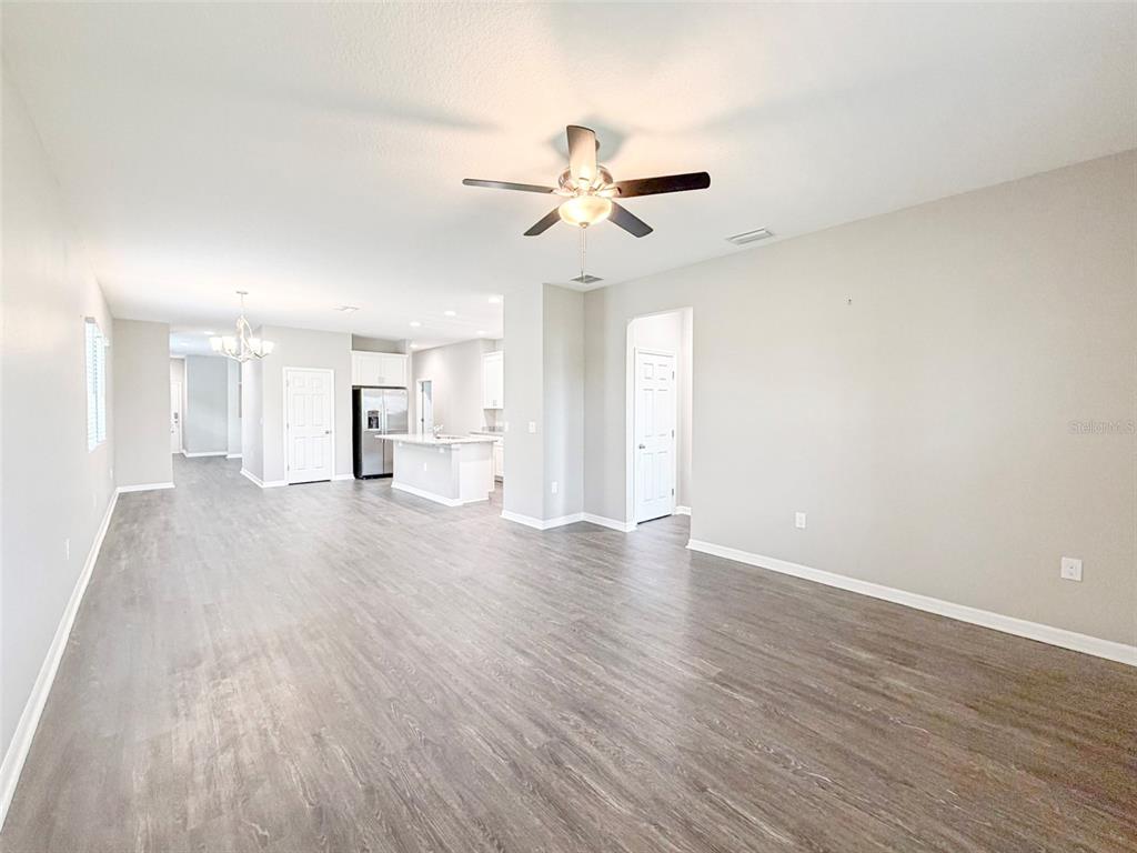 An open-concept living area features light gray walls, wood-look flooring, and a kitchen in the background — 3430 CUP DRIVE, LAKELAND, FL