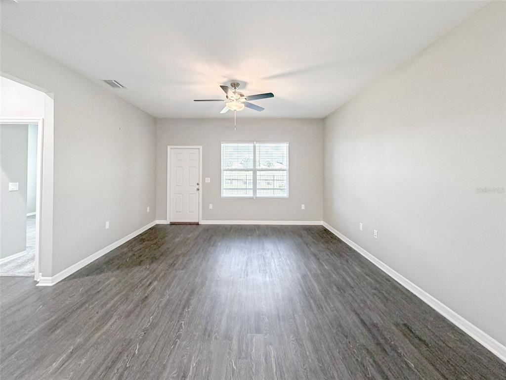 An empty living room features gray walls, dark wood-look flooring, and a ceiling fan — 3430 CUP DRIVE, LAKELAND, FL