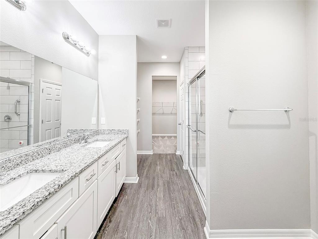 A bathroom features a double vanity with granite countertops, a glass shower, and wood-look flooring — 3430 CUP DRIVE, LAKELAND, FL