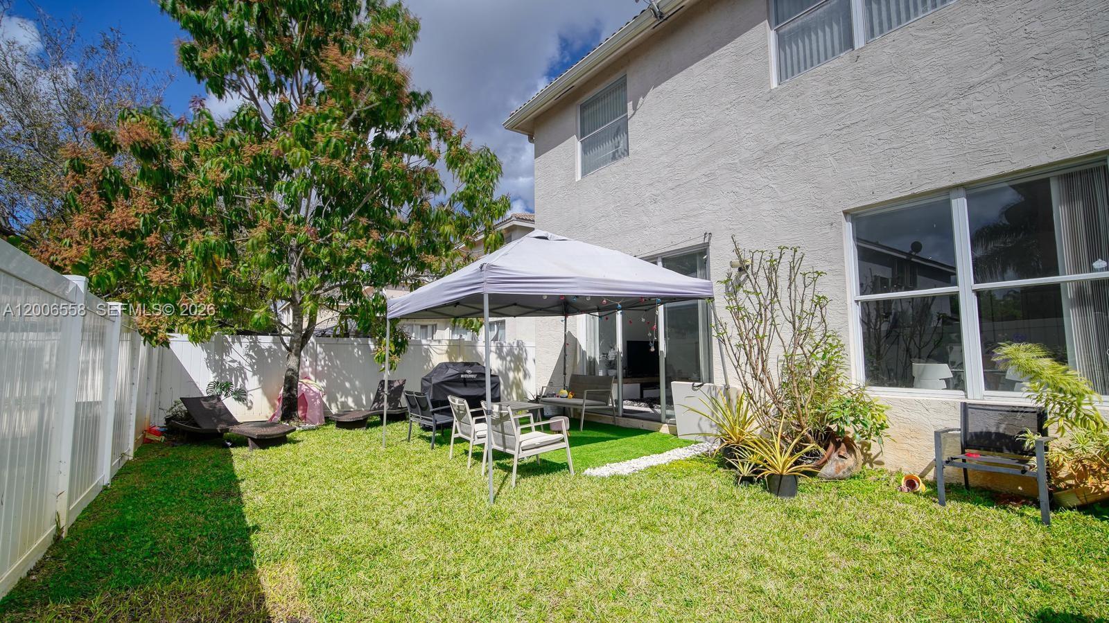 A backyard features a grass lawn, a pop-up canopy, patio furniture, and a white fence — 16388 SW 28th St, Miramar FL 33027, MIRAMAR, FL
