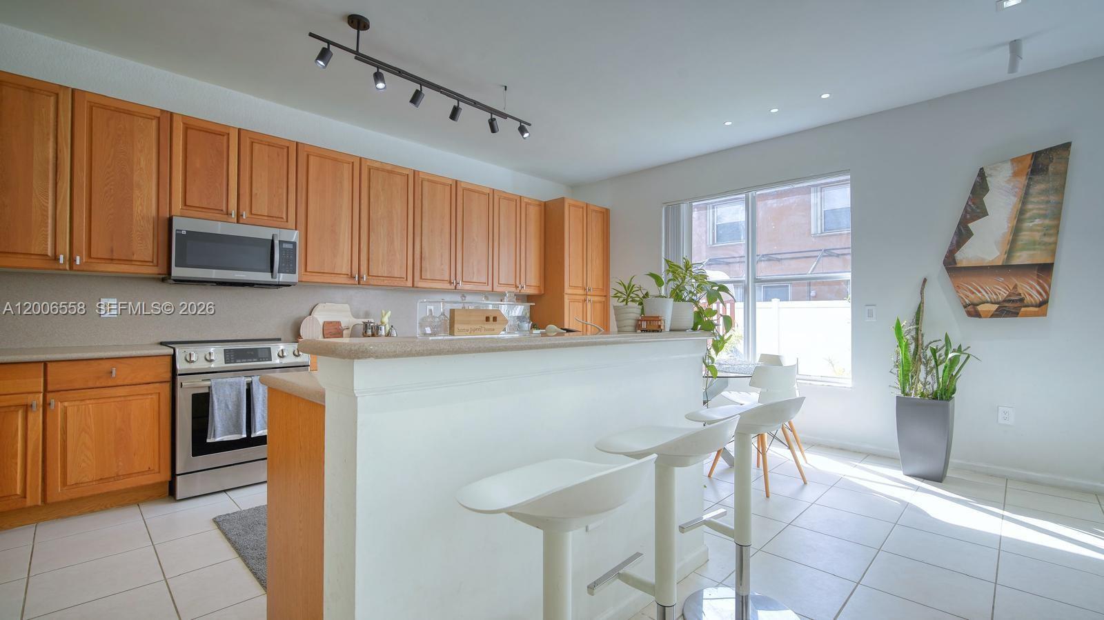 A kitchen features light wood cabinets, a white breakfast bar with stools, and tile flooring — 16388 SW 28th St, Miramar FL 33027, MIRAMAR, FL