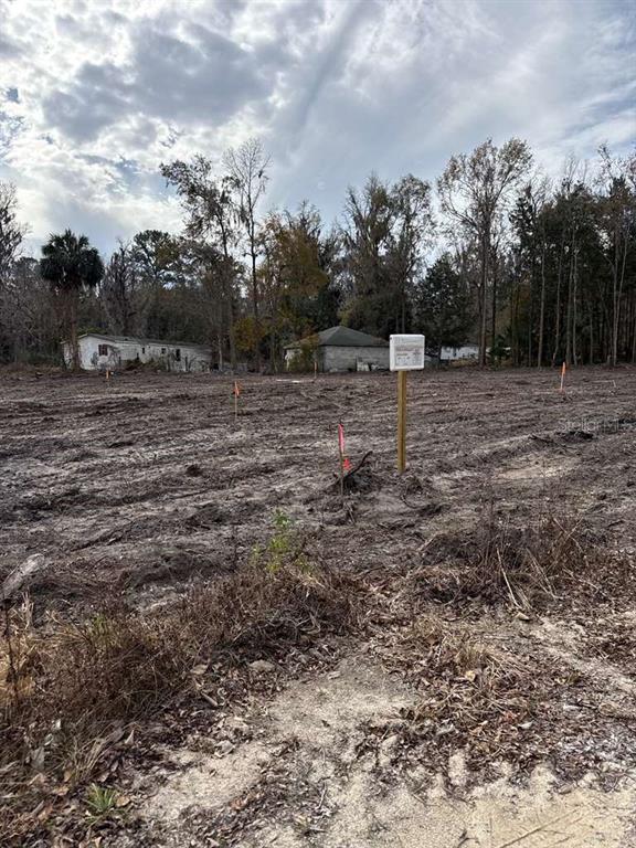 A cleared, vacant lot features several survey stakes and a sign on a wooden post — 0000 Sw 14th ST ROAD, OCALA, FL