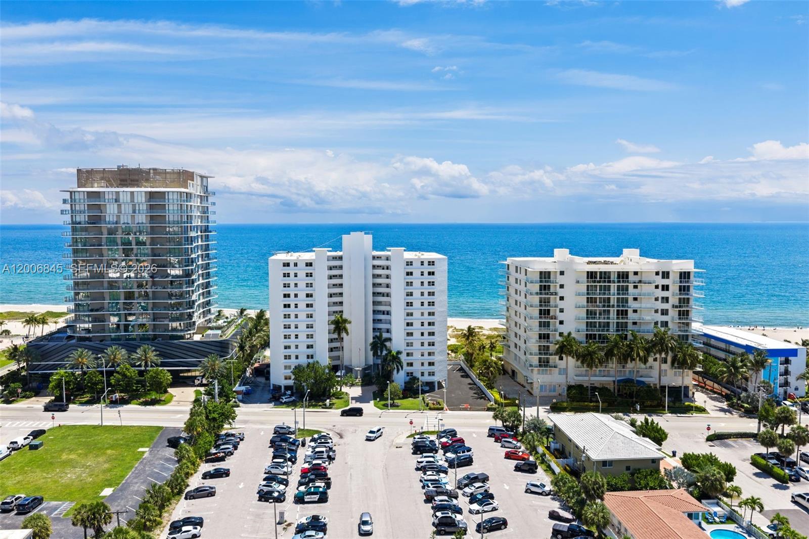 An aerial view shows three beachfront high-rise buildings and a large parking lot — 710 N Ocean Blvd # 1010, Pompano Beach FL 33062, POMPANO BEACH, FL