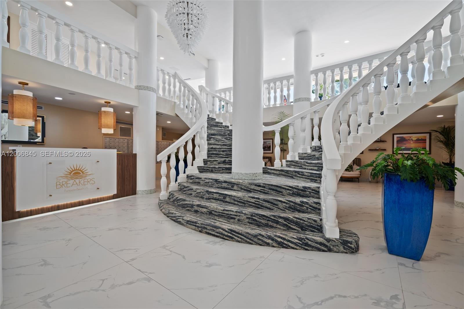 A grand lobby features a curved staircase with patterned carpet and white balustrades — 710 N Ocean Blvd # 1010, Pompano Beach FL 33062, POMPANO BEACH, FL