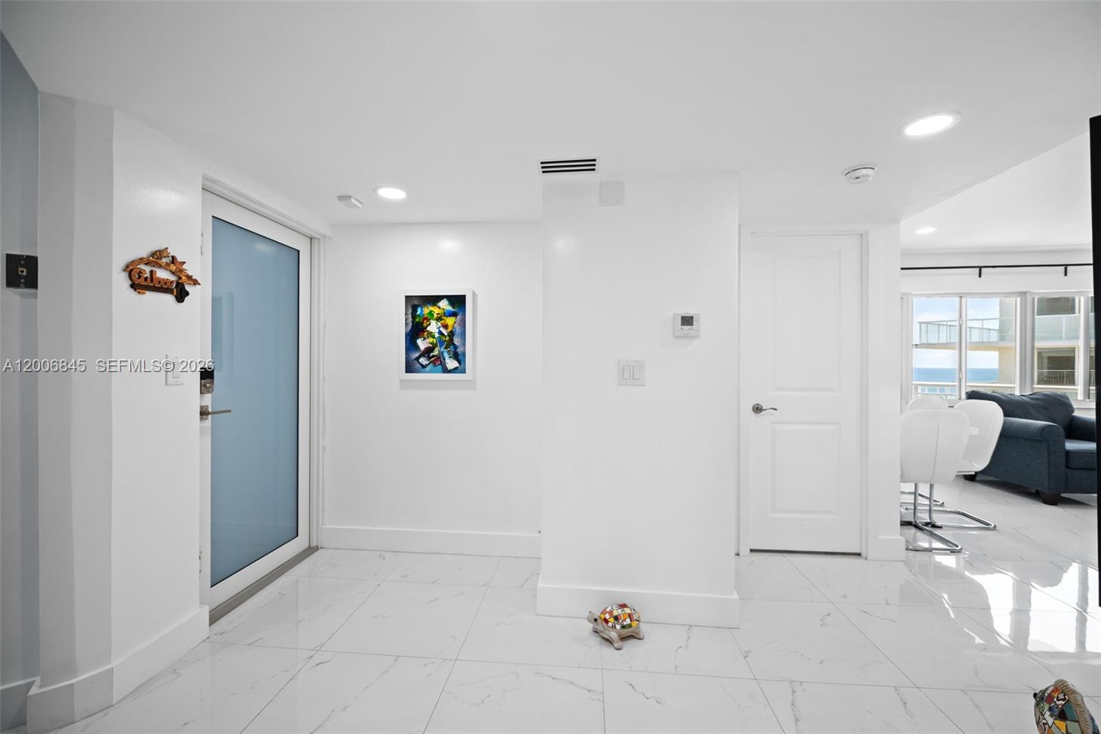 A white-walled entryway features a blue-tinted glass door, white tile flooring, and a closed door — 710 N Ocean Blvd # 1010, Pompano Beach FL 33062, POMPANO BEACH, FL