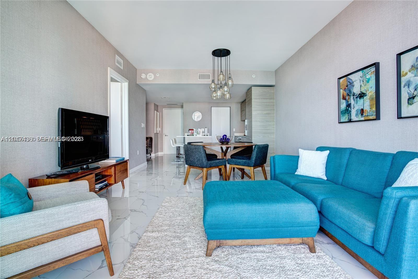 A living room features a blue sofa, a matching ottoman, and a dining area — 1300 S Miami Ave # 2104, Miami FL 33130, MIAMI, FL