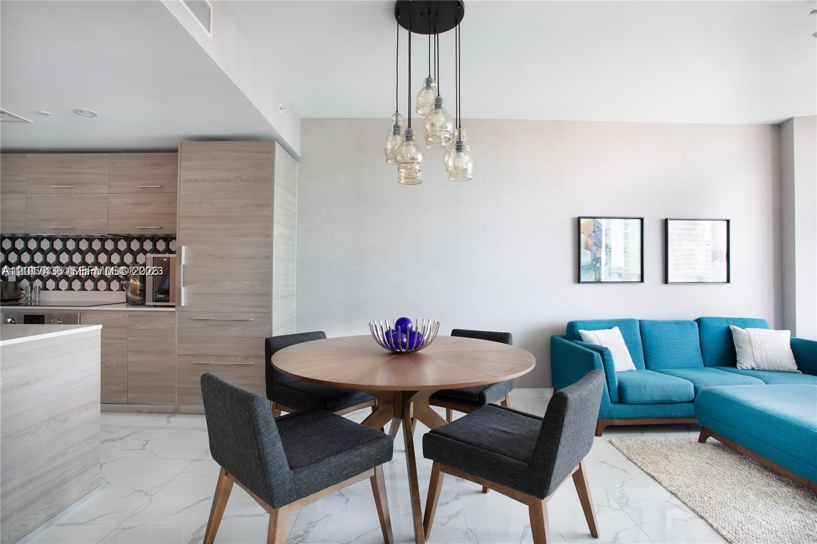 A dining area with a round wooden table and chairs sits beside a blue sofa — 1300 S Miami Ave # 2104, Miami FL 33130, MIAMI, FL