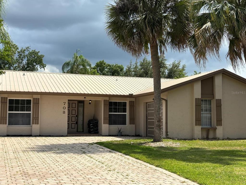 A single-story house with a beige exterior, metal roof, and a paved driveway — 708 DUFFER LANE, KISSIMMEE, FL