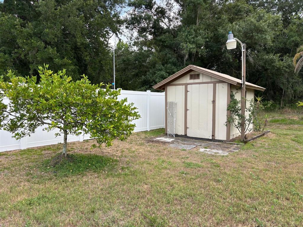 A backyard features a small storage shed, a white vinyl fence, and a citrus tree — 708 DUFFER LANE, KISSIMMEE, FL