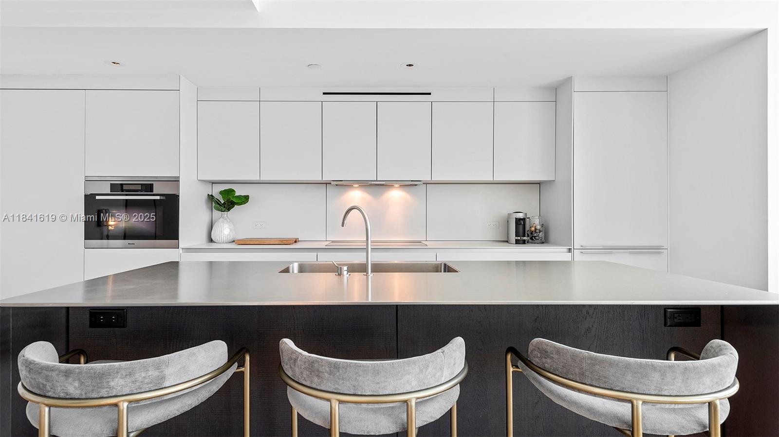 A modern kitchen features a dark wood island with grey stools and white cabinetry — 2901 Collins Ave # 1403, Miami Beach FL 33140, MIAMI BEACH, FL