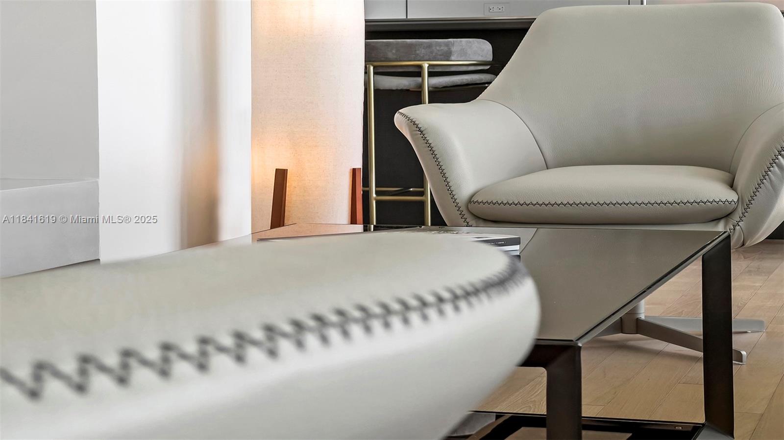 A modern living room features a light-colored armchair, a glass coffee table, and wood flooring — 2901 Collins Ave # 1403, Miami Beach FL 33140, MIAMI BEACH, FL