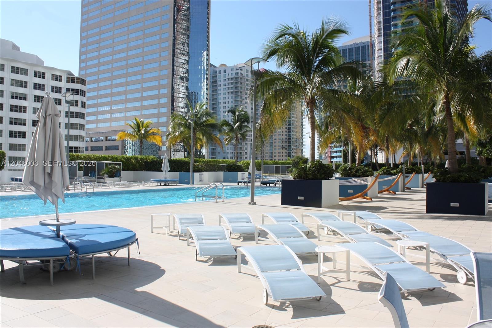 A swimming pool area features lounge chairs, palm trees, and surrounding high-rise buildings — 951 Brickell Ave # 4006, Miami FL 33131, MIAMI, FL