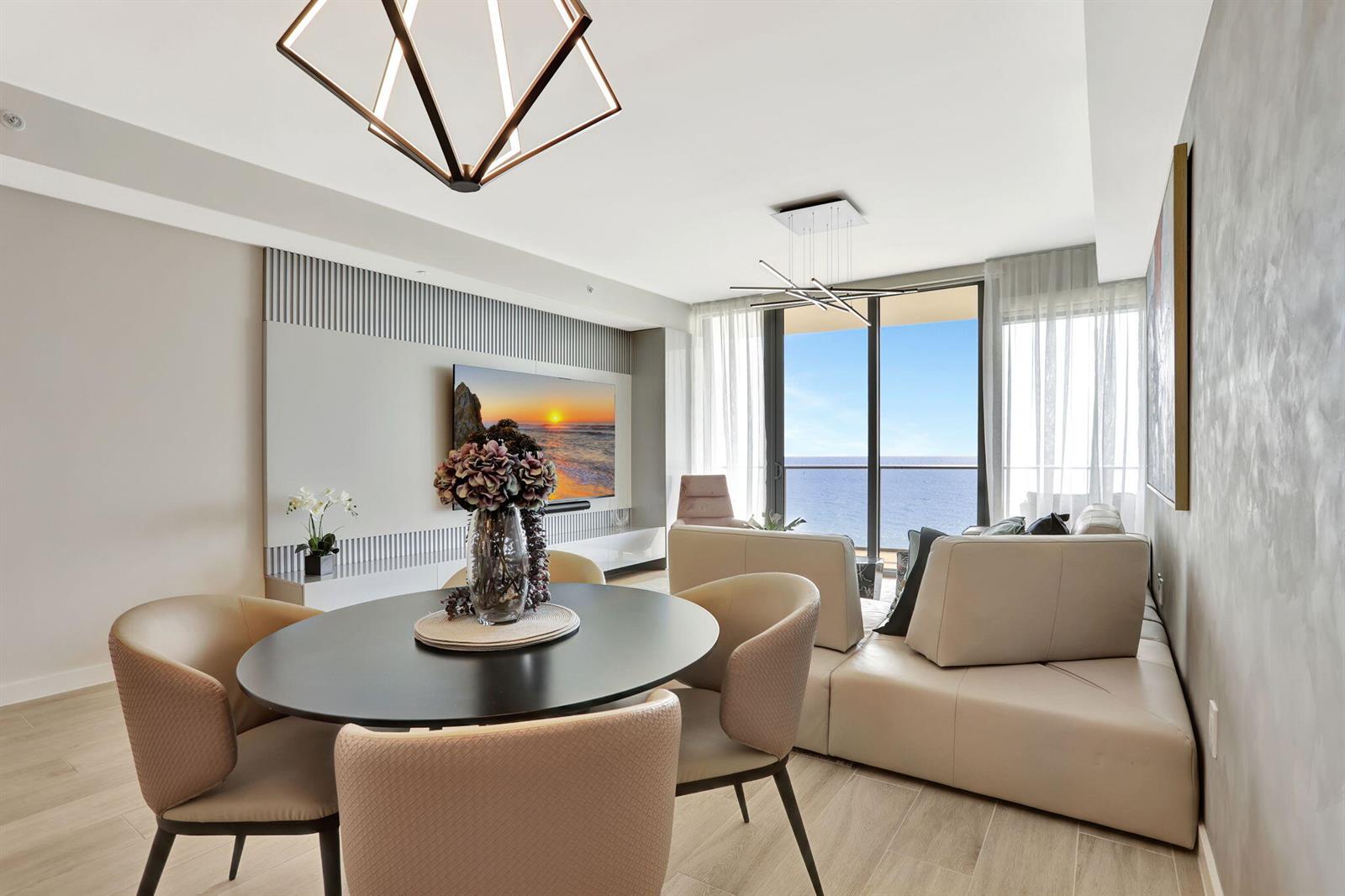 A modern living and dining area features a round table, sofa, and ocean view balcony — 1116 N Ocean Boulevard # 1102, Pompano Beach FL 33062, POMPANO BEACH, FL