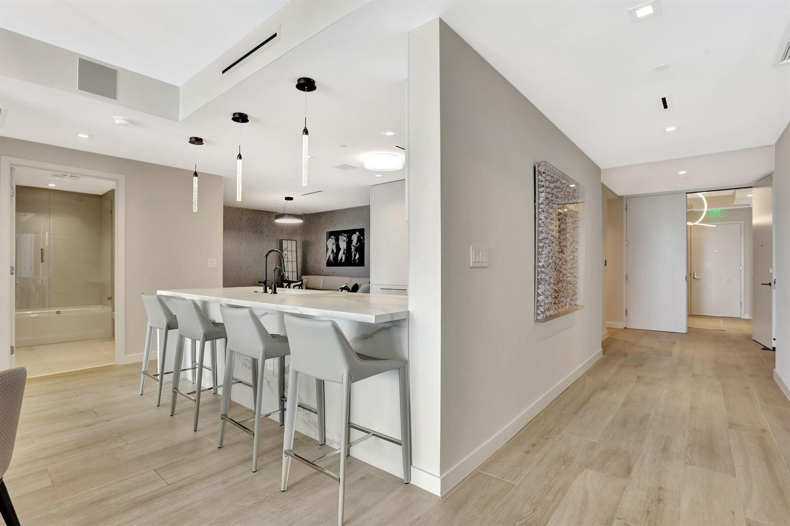 A modern kitchen features a marble-topped island with four gray bar stools and light flooring — 1116 N Ocean Boulevard # 1102, Pompano Beach FL 33062, POMPANO BEACH, FL