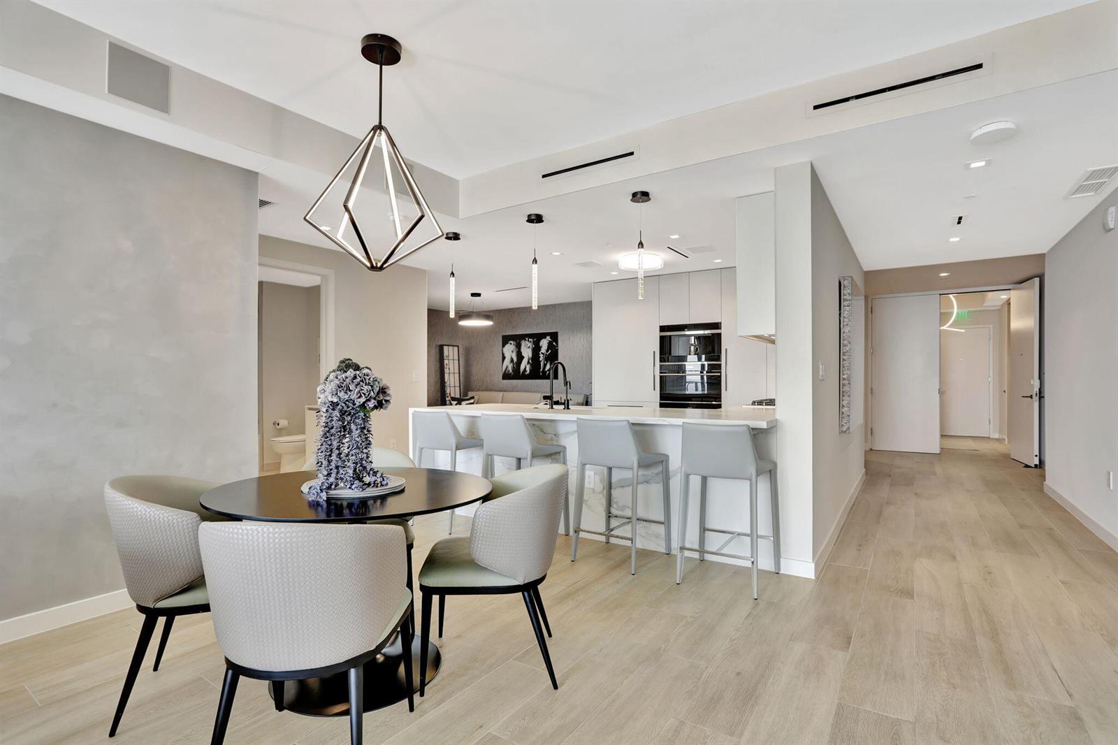 A modern dining area and kitchen feature a geometric pendant light, bar seating, and wood flooring — 1116 N Ocean Boulevard # 1102, Pompano Beach FL 33062, POMPANO BEACH, FL