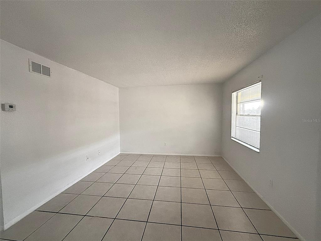 An empty room with white walls, a single window with blinds, and light-colored tile flooring — 720 MICHIGAN COURT UNIT 4, ST CLOUD, FL
