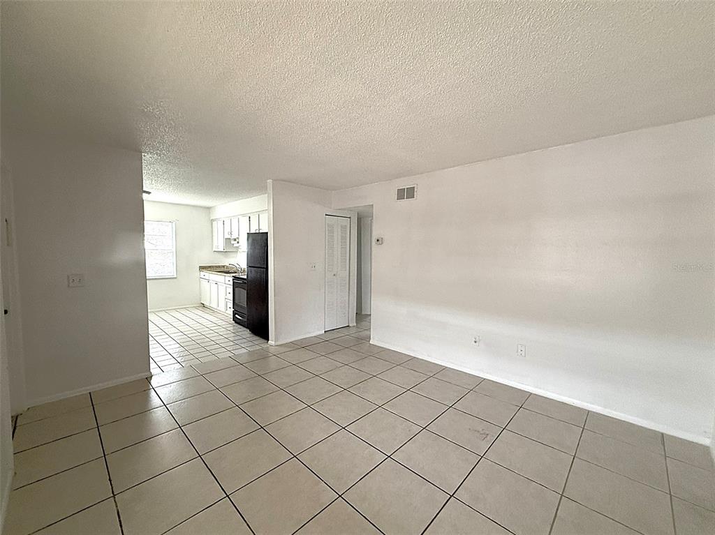 An open-concept living area with light-colored floor tiles leads into a kitchen with white cabinets — 720 MICHIGAN COURT UNIT 4, ST CLOUD, FL