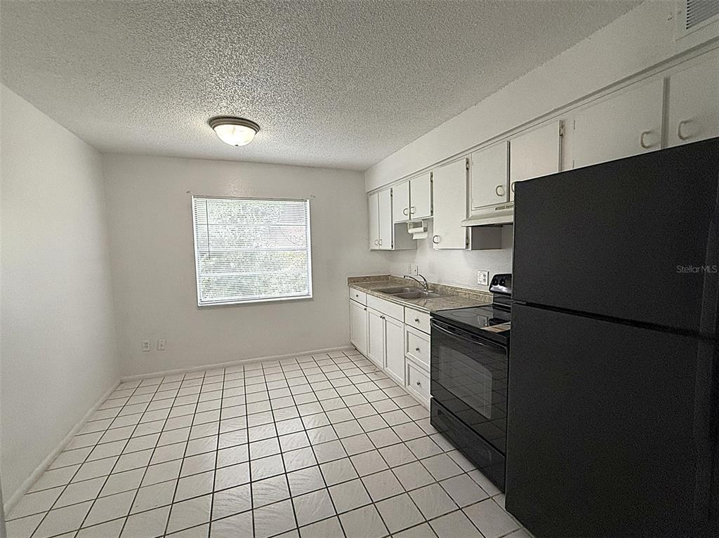 A kitchen features white cabinets, a black refrigerator, a black stove, and white floor tiles — 720 MICHIGAN COURT UNIT 4, ST CLOUD, FL