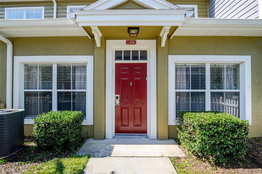 A red front door with a unit number sign is centered between two large windows — 2610 LODI CIRCLE UNIT 106, KISSIMMEE, FL
