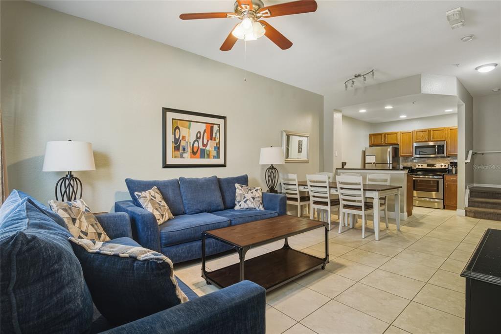 A living room with blue sofas and a coffee table opens to a dining area — 2610 LODI CIRCLE UNIT 106, KISSIMMEE, FL