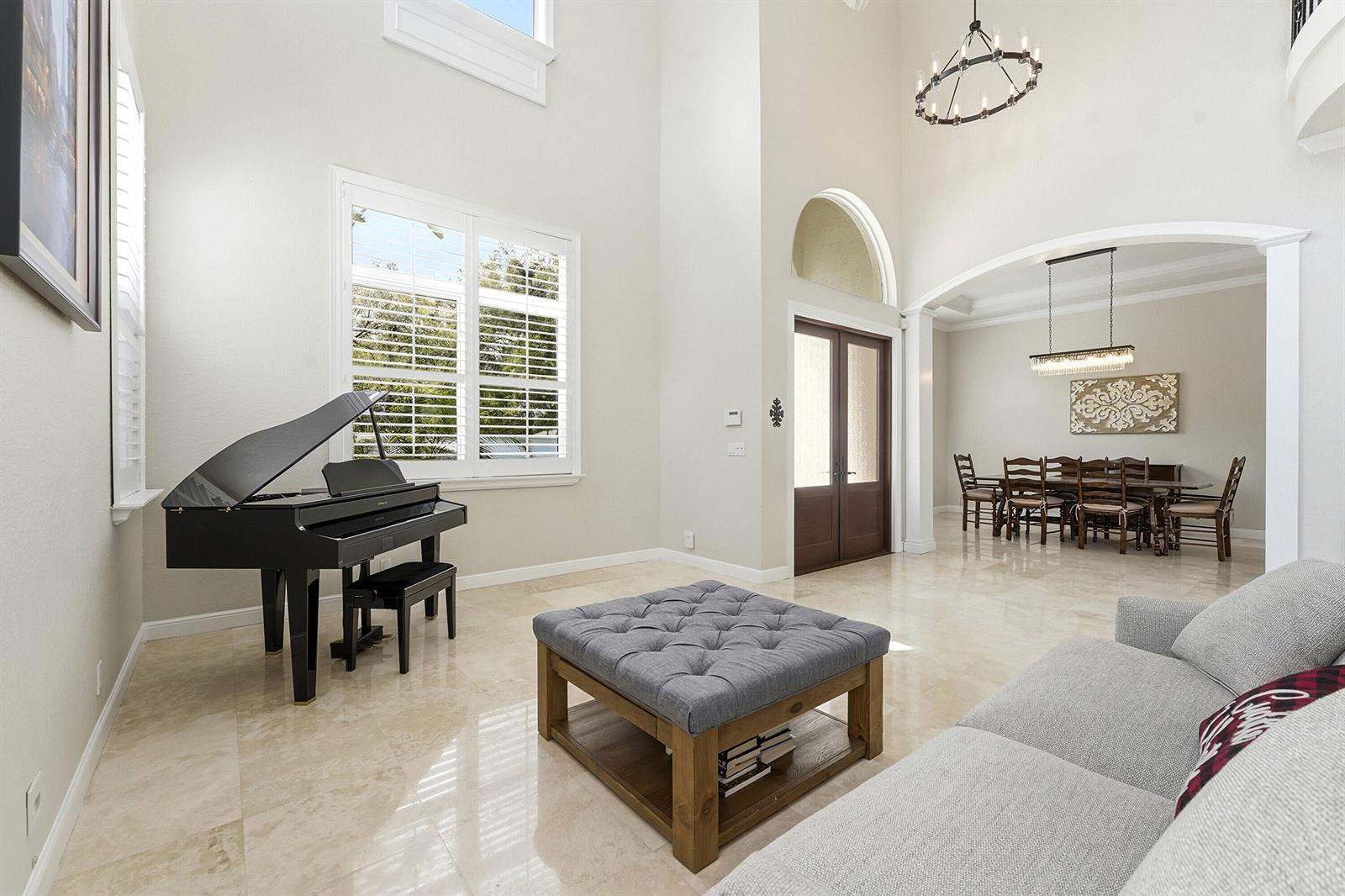 A living room with a grand piano, tufted ottoman, and an adjacent dining area — 5038 NW 24th Circle, Boca Raton FL 33431, BOCA RATON, FL