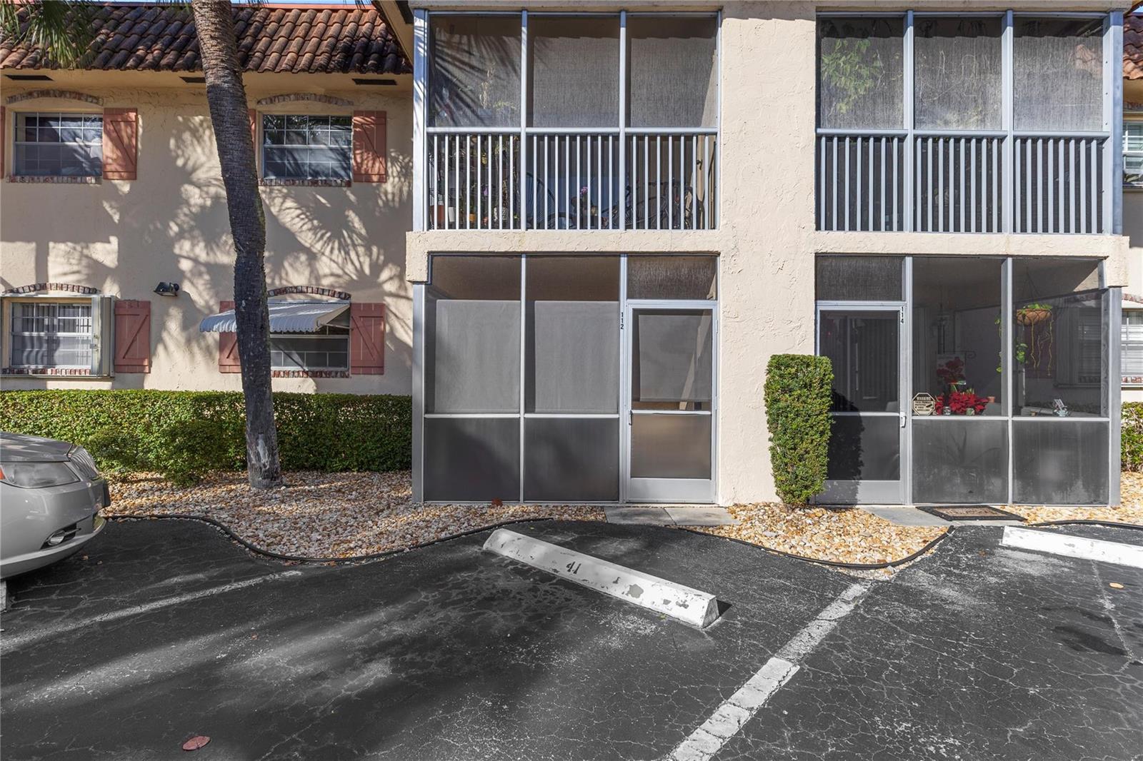 The exterior of a two-story apartment building features screened-in patios and assigned parking spaces — 101 E Mcnab Road # 112, Pompano Beach FL 33060, POMPANO BEACH, FL