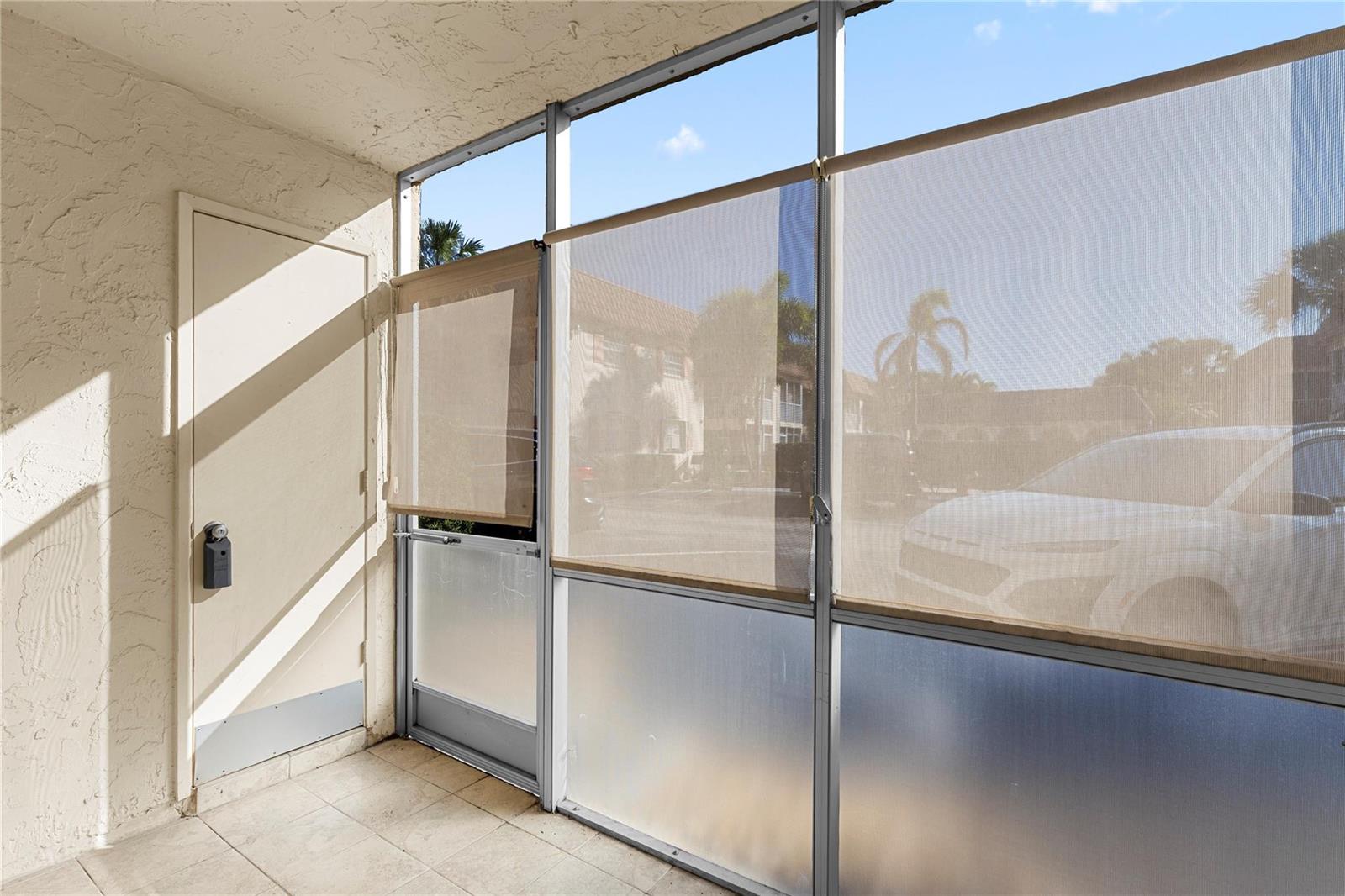A covered patio features tiled flooring, a metal door, and large windows with privacy shades — 101 E Mcnab Road # 112, Pompano Beach FL 33060, POMPANO BEACH, FL