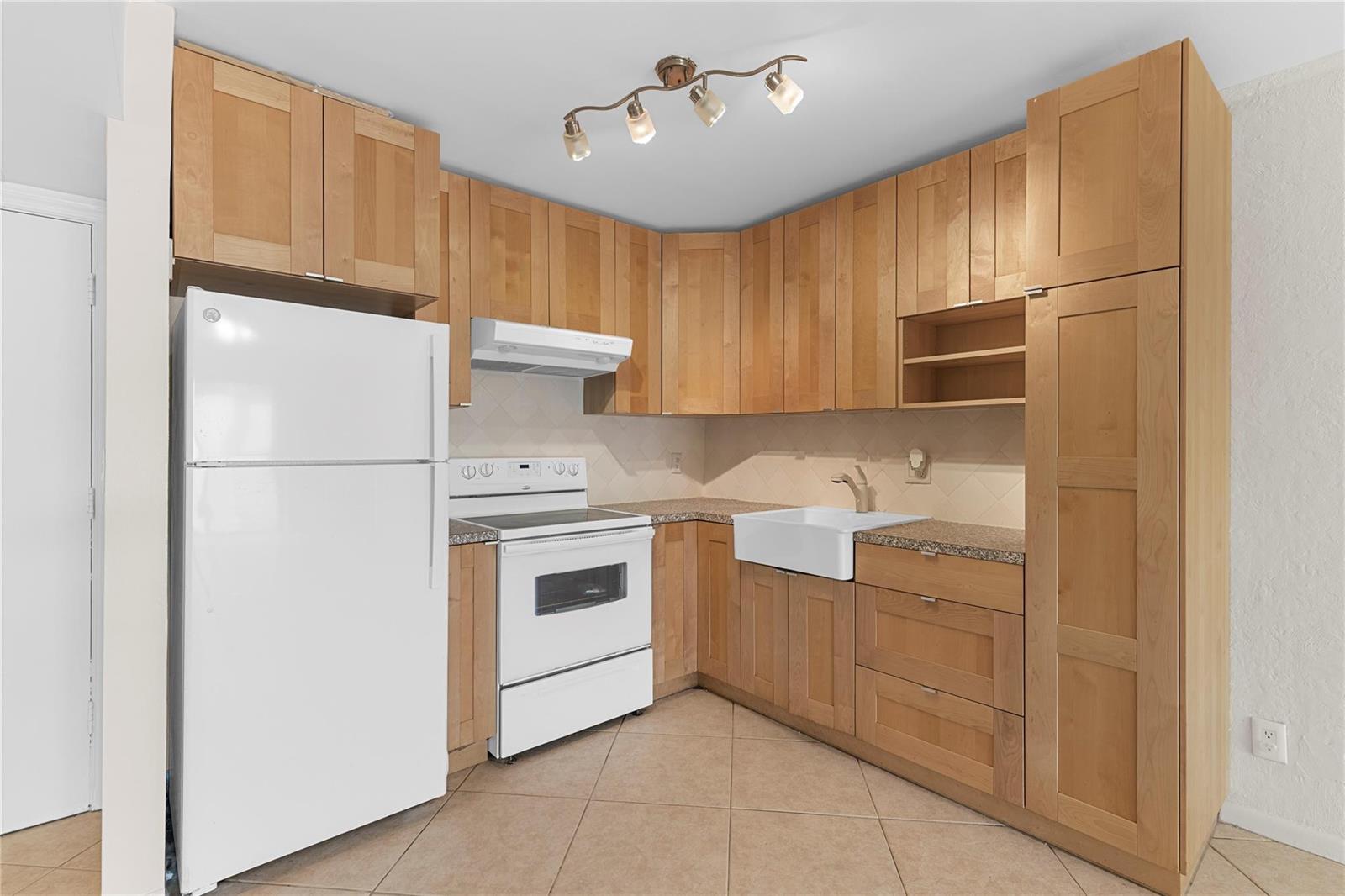 A kitchen features light wood cabinets, a white refrigerator, a white stove, and tile flooring — 101 E Mcnab Road # 112, Pompano Beach FL 33060, POMPANO BEACH, FL