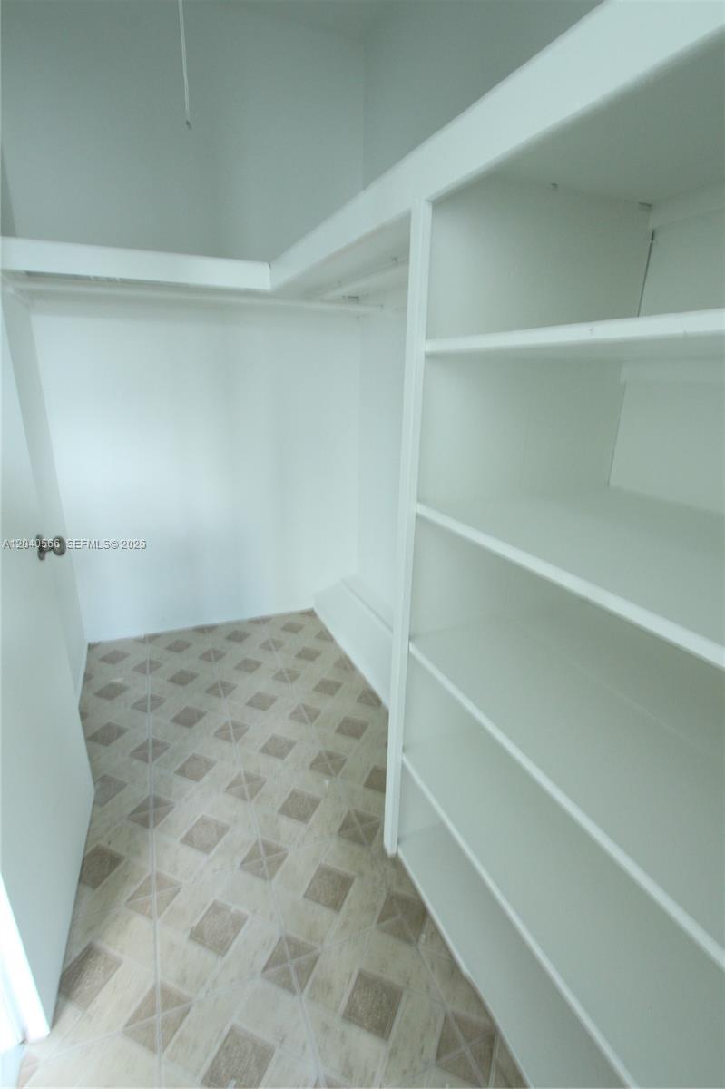 A walk-in closet features white shelving, a hanging rod, and light-colored patterned floor tiles — 1115 Euclid Ave # 11, Miami Beach FL 33139, MIAMI BEACH, FL