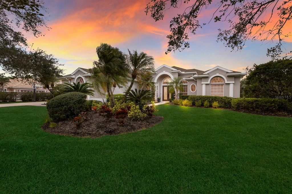 A single-story house with a manicured lawn, palm trees, and a sunset sky — 9405 BOXTHORN PLACE, BRADENTON, FL